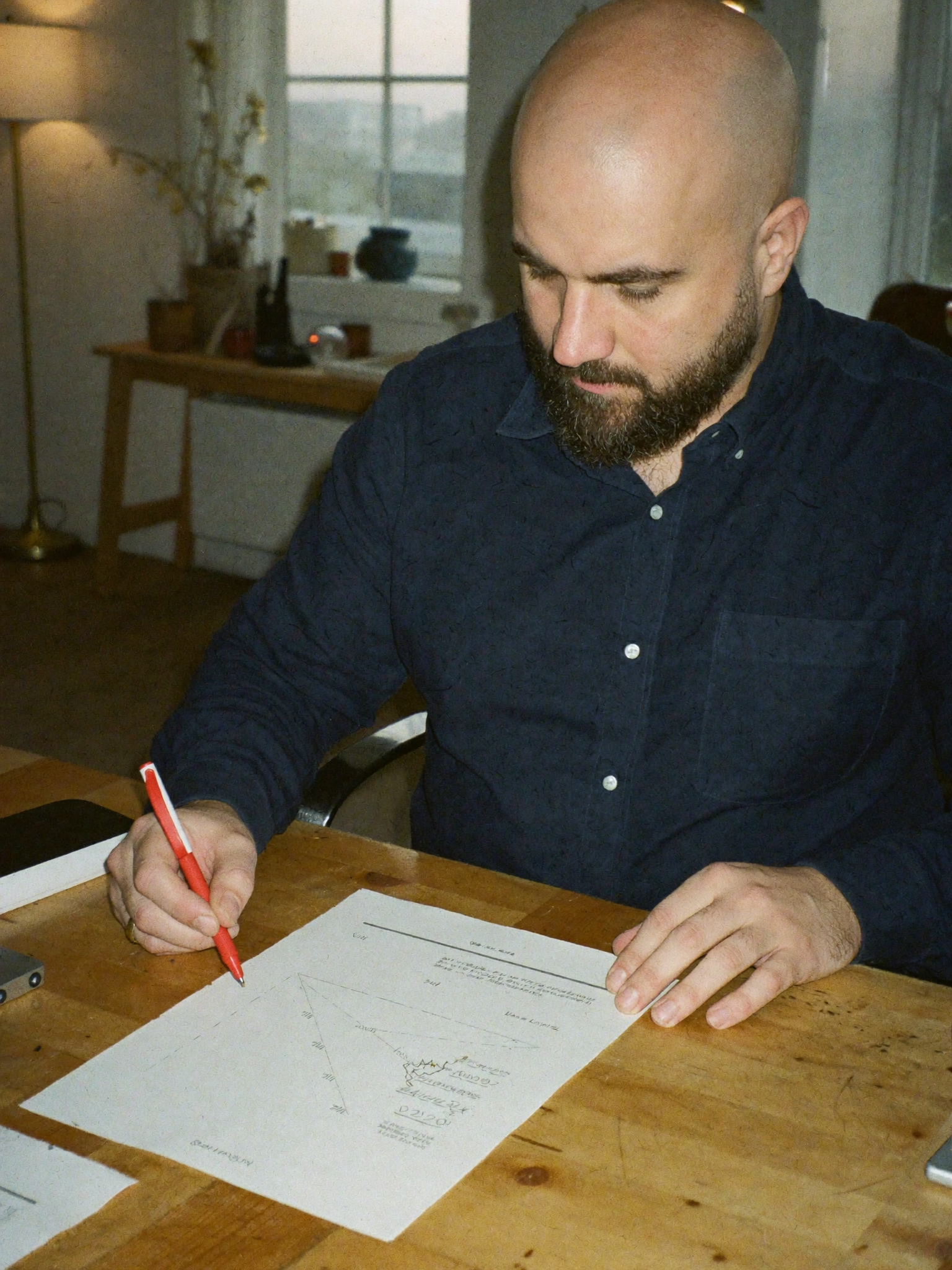 John Marston sketching a process diagram in a notebook at a wooden desk